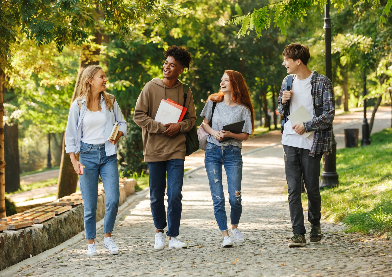 Vier Studierende mit Büchern auf einem Weg im Grünen